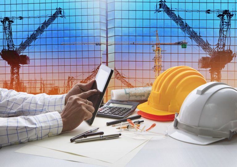 hand of architect working on table with tablet computer and working tool equipment against reflection of office building and crane construction use for civil engineering and construction industry business